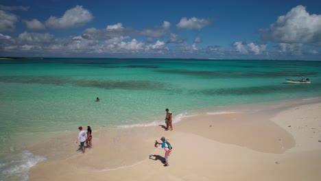 Drone-turn-around-cayo-de-agua-sandbar,-couple-walk-on-sand-beach-to-caribbean-sea