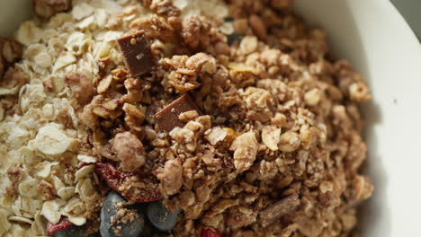 Close-up-of-a-breakfast-bowl-with-granola,-chocolate,-and-berries-on-a-table