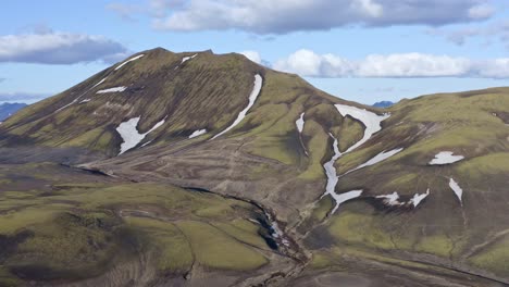 Aerial-drone-view-with-a-backward-left-movement,-facing-a-green-mountain-in-Landmannalaugar-near-Bláhylur-Lake