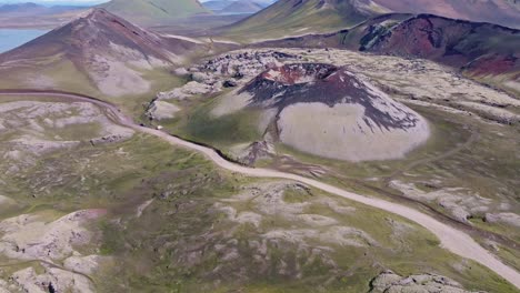 Aerial-drone-view-with-a-bottom-to-top-reveal-movement,-focusing-on-Stutur-Crater-with-the-Landmannalaugar-mountains-in-the-background