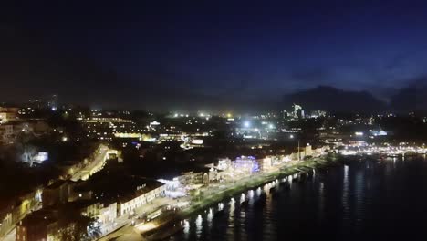 Tilt-down-aerial-shot-of-Gaia-at-night-along-the-riverfront,-Portugal