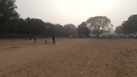 Eine-Gruppe-Von-Leuten,-Die-Cricket-In-Indien,-Gurgaon,-Sektor-29,-Leisure-Valley-Auf-Einem-Sonnigen,-Aber-Nebligen-Und-Sandigen-Spielplatz-Spielen