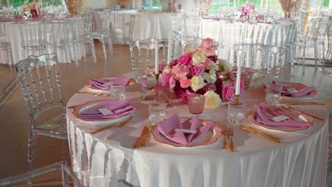 Shot-of-fancy-wedding-reception-tables-with-glasses-and-plates,-table-is-decorated-with-gorgeous-pink-and-white-roses-and-white-candles,-rotating-shot