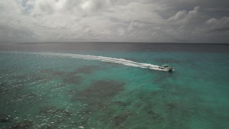 Speedboat-cruising-on-turquoise-waters-of-Los-Roques,-Venezuela-with-clouds-above,-aerial-view