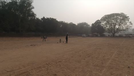A-group-of-people-playing-cricket-in-India,-Gurgaon,-sector-29,-leisure-valley-in-a-sunny-but-foggy,-and-sandy-playground