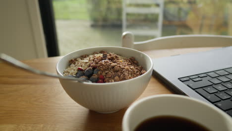 Well-lit-granola-bowl-on-lunch-break-with-coffee-and-laptop-on-wooden-table