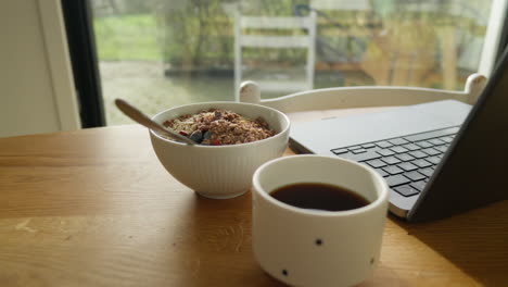 Breakfast-scene-with-cereal-bowl,-coffee,-and-laptop-on-a-wooden-table