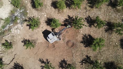 Drone-view-of-digger-working-among-trees-in-agricultural-land,-landscaping
