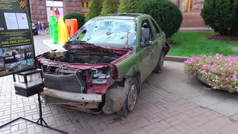 Shelled-green-car-on-Khreshchatyk-main-street-from-the-Russia-Ukraine-war-in-Kyiv-city-center,-destroyed-broken-war-vehicle-in-Ukraine,-4K-shot