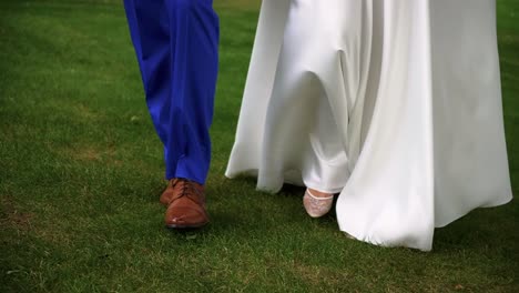 Closeup-shot-of-the-legs-of-bride-and-groom-walking-together-on-the-grass-in-the-park-on-the-sunny-wedding-day