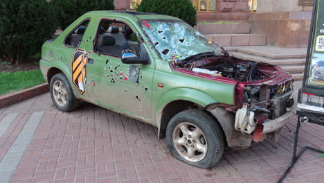 Shelled-green-car-on-Khreshchatyk-main-street-from-the-Russia-Ukraine-war-in-Kyiv-city-center,-destroyed-war-vehicle-in-Ukraine,-4K-shot