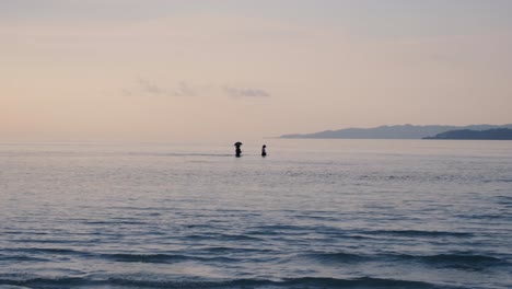 Un-Pequeño-Grupo-De-Mujeres-Con-Sombrilla-Para-Protegerse-Del-Sol-Caminando-A-Través-De-Una-Laguna-Oceánica-Entre-Dos-Islas-Tropicales-Durante-La-Marea-Baja.
