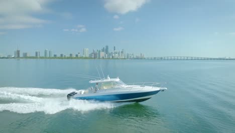 The-yacht,-moving-through-the-blue-green-sea,-is-accompanied-by-white-waves-and-a-clear-blue-sky-above-the-city-of-Miami