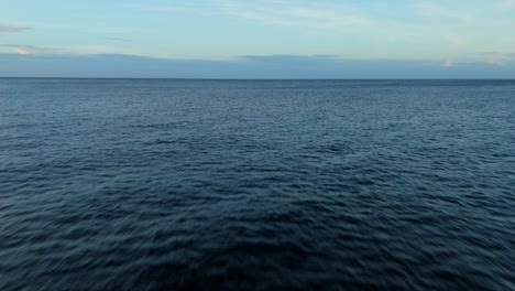 Aerial-dolly-out-to-sea-with-clouds-on-horizon,-vibrant-dark-blue-hue-on-water-currents