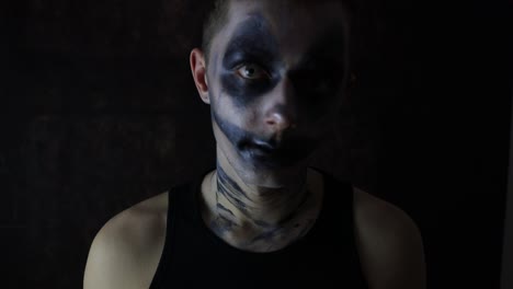 Young-man-with-a-scary-Halloween-dark-clown-makeup-standing-in-front-of-a-black-background