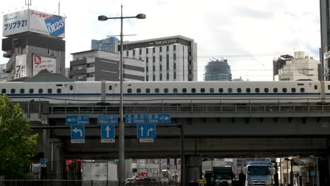 N700-Tokaido-Shinkansen-Fährt-Auf-Erhöhter-Strecke-Im-Bezirk-Shinbashi-In-Minato-Vorbei,-Darunter-Fährt-Täglicher-Verkehr-Vorbei
