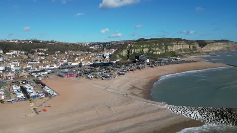Aerial-drone-shot-of-Hastings-UK,-High-Orbiting-shot-of-the-Land-Based-Fishing-Fleet-of-Beach,-Old-Town-and-East-Hill-Cliffs