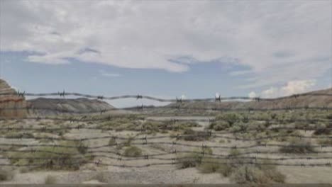 Hochwertige-3D-CGI-Aufnahmen,-Die-In-Einer-Wüstenszene-über-Einen-Maschendrahtzaun-Auf-Die-Militäranlage-Area-51-Steigen,-Mit-Einem-UAP-UFO,-Das-Mit-Hoher-Geschwindigkeit-Aus-Den-Fernen-Wolken-Auftaucht-Und-über-Uns-Hinwegzoomt