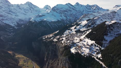 Vista-Aérea-De-Un-Pequeño-Pueblo-Nevado-De-Suiza-Cerca-Del-Empinado-Borde-De-La-Montaña