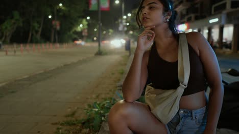 Fashionable-Woman-squatting-on-a-sidewalk-at-night-with-city-lights-behind