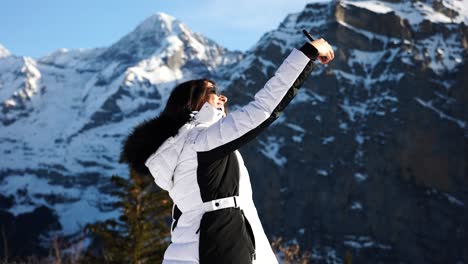 Young-brunette-female-hold-phone-and-take-selfies-with-Switzerland-mountains