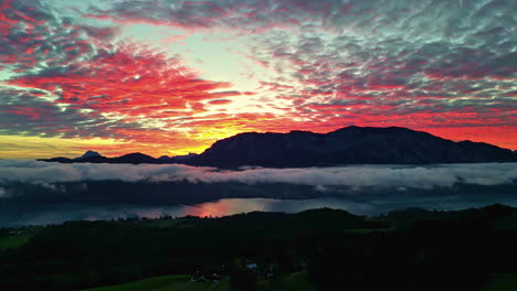 Epic-fire-sunset-mountains-and-fog-layer-above-lake,-panoramic-aerial-establishing-background