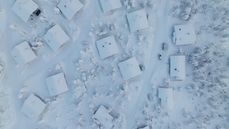 Snowy-cottage-in-mountain-forest,-winter-in-Lapland---Birds-eye,-drone-shot