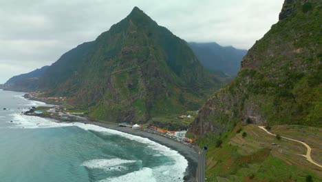 Aerial-view-of-mountains-on-Madeira-Island-with-waves-and-coastline-with-buildings-during-cloudy-day