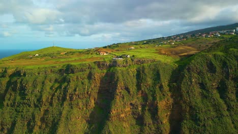 Drone-approaching-shot-of-green-cliff-with-a-few-houses-on-top-of-Madeira-Island