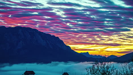 Fire-sunset-of-vibrant-red-light-reflecting-on-clouds-from-orange-sky-above-scenic-mountains-and-thick-fog-layer
