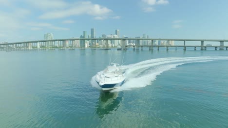 A-beautiful-yacht-sails-away-from-the-bridge-near-Miami-across-the-blue-green-sea,-leaving-behind-traces-of-foamy-white-waves