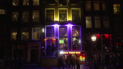 Static-shot-of-The-Black-Tiger-Bar-in-Amsterdam-during-nighttime,-pedestrians-walking-around-city-streets