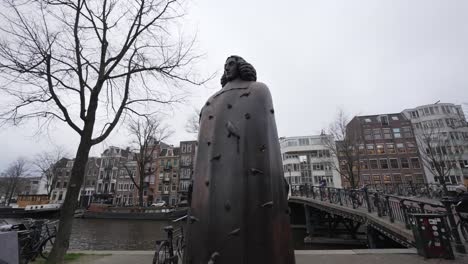 Low-angle-shot-of-statue-in-Amsterdam-with-pedestrians-crossing-bridge-over-the-canal