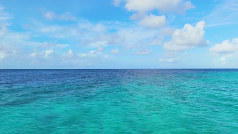 Coral-reef-with-sandy-waters-under-blue-sky-with-fluffy-clouds