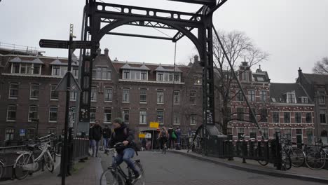 Gente-Cruzando-El-Puente-En-Ámsterdam-Sobre-El-Canal-Del-Centro-De-La-Ciudad.
