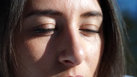 Close-up-of-sunshine-illuminated-female-face,-brown-hair-and-eyes-blink