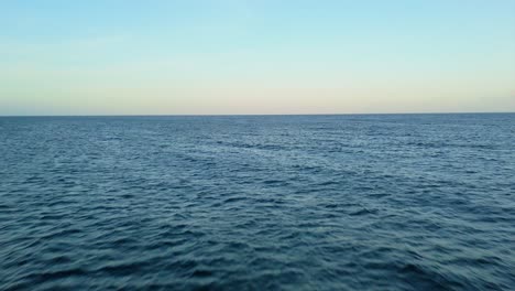 Soft-sunset-light-glows-on-horizon-as-drone-flies-above-open-ocean-deep-blue-water