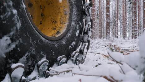 Chained-excavator-wheels-move-through-snowy-forest,-close-up