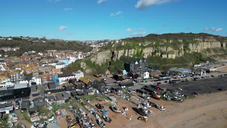 Aerial-drone-shot-of-Hastings-UK,-camera-flying-over-the-Stade-Beach,-fishing-boats-and-high-street,-towards-the-East-Hill-Cliff-Railway