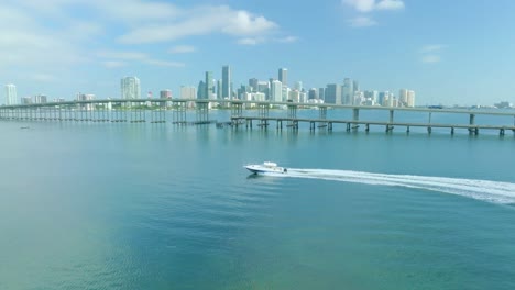 The-yacht-is-sailing-alongside-the-bridge-across-the-blue-sea,-with-the-city-of-Miami,-Florida,-in-the-background