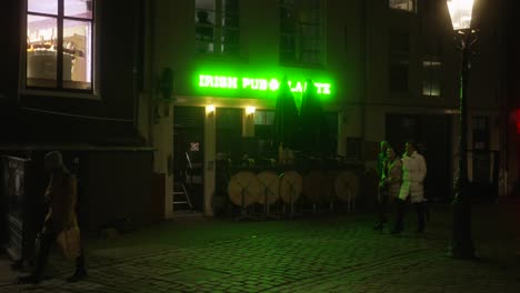 Irish-pub-entrance-with-green-advertisement-illimuniating-street-with-pedestrians-walking