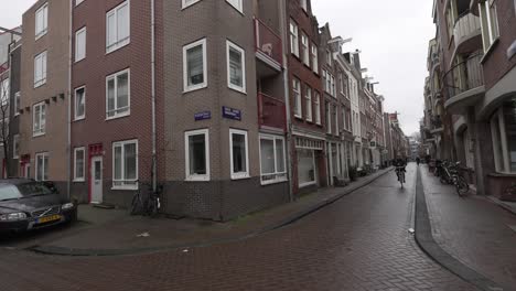 Street-in-Amsterdam,-Residential-buildings,-bicycle-cycling-through-neighbourhood