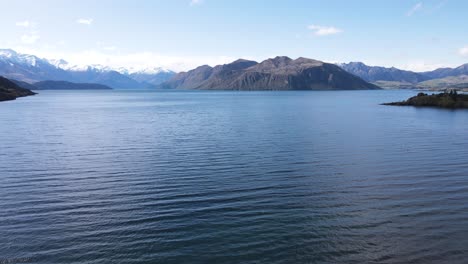 Sweeping-panoramic-shot-capturing-the-vast-expanse-of-Lake-Wanaka,-showcasing-its-crystal-clear-blue-waters-and-the-surrounding-mountains