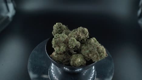 Green-Dried-Marijuana-Buds-Close-Up-Shot,-pile-of-dried-marijuana-plants-in-a-shiny-bowl,-trichomes-strains,-on-a-reflecting-rotating-stand,-studio-lights,-cinematic-zoom-out-slow-motion-120-fps