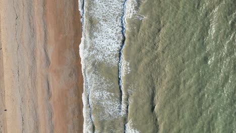 Drone-shot-of-Hastings-UK,-top-down-shot-flying-over-Hastings-beach,-Waves-crashing-into-sandy-shore-lined-beach