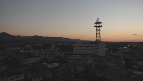Dusk-settles-over-a-town-with-a-prominent-communication-tower-silhouetted-against-a-fading-sky-in-Izumi,-Kyushu,-Japan