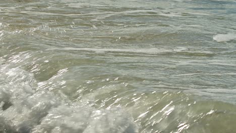 Closeup-of-frothy-water-from-ocean-waves-crashing-as-it-pulls-back-across-wet-sand