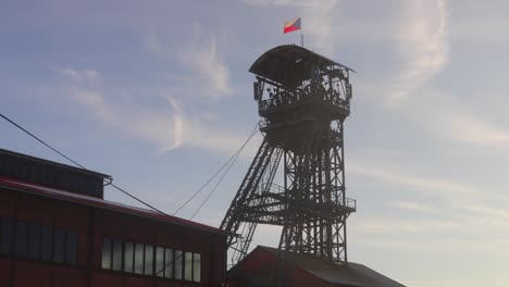 Alter-Industrieturm-Mit-Einer-Tschechischen-Flagge-An-Der-Spitze,-Der-Neben-Einem-Roten-Backsteingebäude-Unter-Klarem-Himmel-Steht