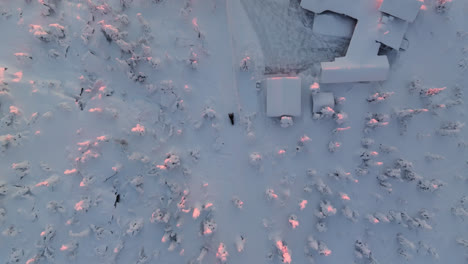 Birds-eye-drone-shot-tracking-skidoo-passing-a-house,-arctic-sunrise-in-Lapland