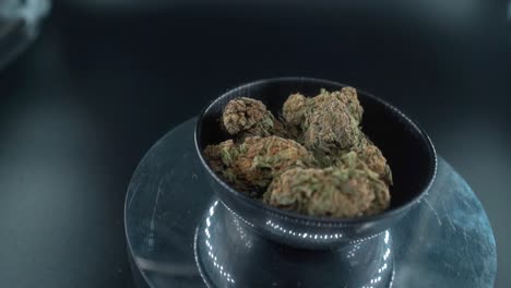 Grayish-Green-Dried-Marijuana-Buds-Close-Up-Shot,-pile-of-dried-marijuana-plants-in-a-shiny-bowl,-trichomes-strains,-on-a-reflecting-rotating-stand,-studio-lights,-crane-rotating-zoom-out-slow-motion